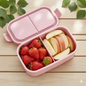 Fresh strawberries and cut apples neatly arranged in the top tier of the pink bento lunch box.